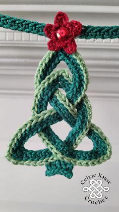 a crocheted christmas ornament hanging from a rope with a red flower on it