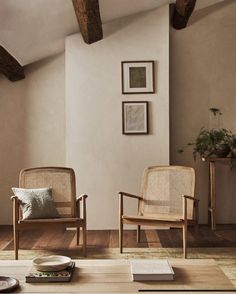 two chairs and a table in a room with wood flooring, framed pictures on the wall