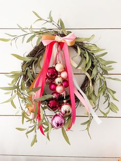 a wreath with ornaments hanging from it on a white wooden wall next to an orange pumpkin