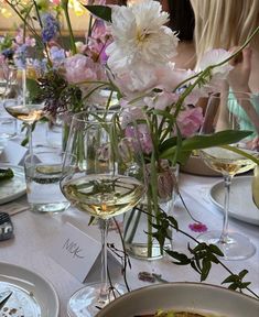 the table is set with wine glasses, plates and flowers in vases on it