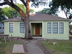 a small green house with a tree in the front yard and picnic table on the lawn