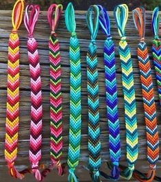 several different colored braided bracelets hanging on a wooden fence with ribbons attached to them