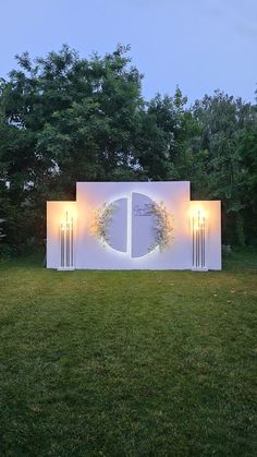 an outdoor ceremony setup with lights and flowers on the back wall, surrounded by lush green grass