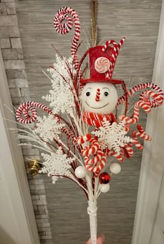 a hand holding a candy cane bouquet with a snowman in the center and candy canes hanging from it