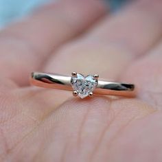 a close up of a person's hand holding a ring with a heart shaped diamond