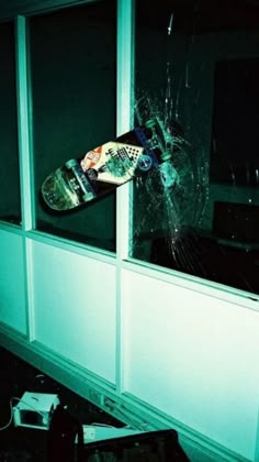 a broken window with a skateboard stuck in it and the glass is cracked off