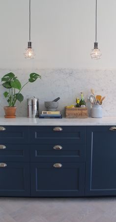 a kitchen with blue cabinets and marble counter tops, hanging lights above the island area