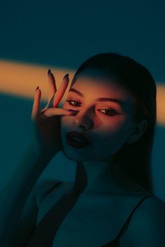 a woman holding her hand up to her face in front of a blue wall with light coming through it