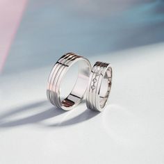 two wedding rings sitting next to each other on top of a white surface with pink and blue background