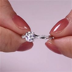 a woman's hand holding a ring with a diamond on the middle of it