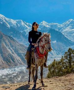 a woman riding on the back of a brown horse next to snow covered mountain tops