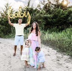 a man and two children holding up the word baby in front of them on a dirt road