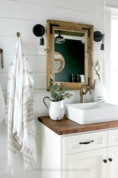 a white sink sitting under a bathroom mirror next to a wooden counter topped with a potted plant