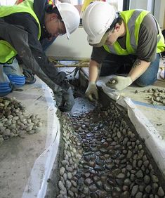 two men in hard hats and safety vests are working on a rock lined area