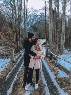 a man and woman standing next to each other in front of trees with snow on the ground