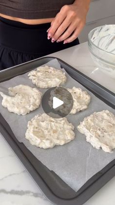 a woman is making cookies on a baking sheet with white icing in the background