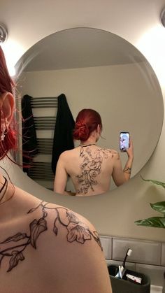 a woman with tattoos taking a selfie in front of a mirror while looking at her cell phone