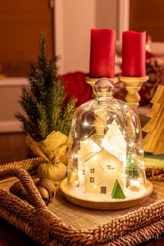 a glass bell jar with a house under it on a wicker tray next to christmas trees