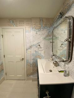 a bathroom with a sink and mirror next to a door that has a map on it