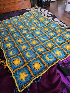 a blue and yellow crocheted blanket sitting on top of a purple bedspread