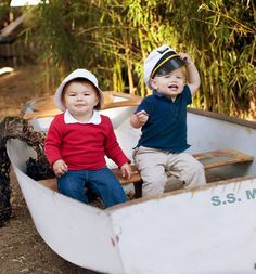 two young boys sitting in a small boat on the ground next to some trees and bushes