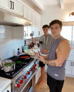 two men standing in a kitchen preparing food on the stove top and cooking with utensils