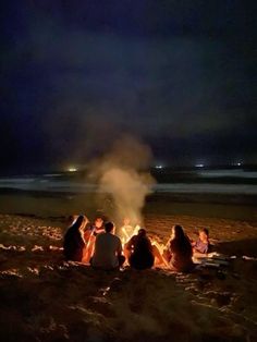 people sitting around a campfire on the beach at night