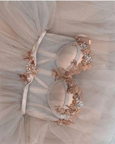 two pairs of shoes are on top of a tulle skirt with gold and crystal decorations