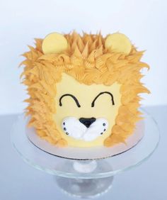 a lion cake with yellow frosting on a clear glass platter and white background