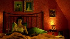 a woman sitting on top of a bed in a room with red walls and paintings