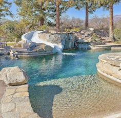 a pool with a slide in it next to some trees and rocks on the ground