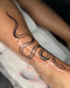 a woman's arm with a snake tattoo on her left leg and the word snake written in cursive writing