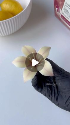 a person in black glove holding up a paper flower next to a bowl of lemons