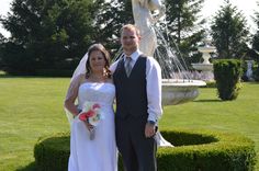 a bride and groom standing in front of a fountain at their wedding ceremony, posing for the camera