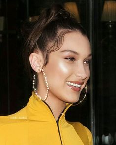 a close up of a person wearing earrings and a yellow jacket with pearls on it