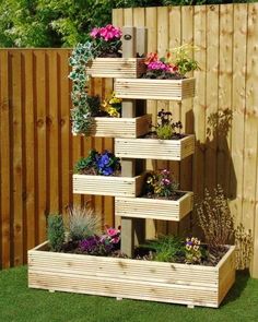 a tall wooden planter filled with lots of flowers next to a fence and green grass