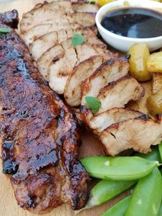 a close up of meat on a cutting board with vegetables and dipping sauce in the background