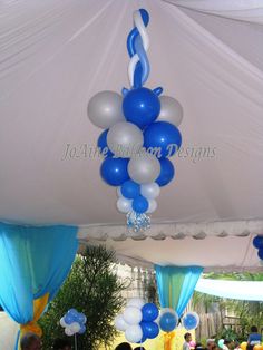 blue and white balloons are hanging from the ceiling in an outdoor party area with people sitting at tables