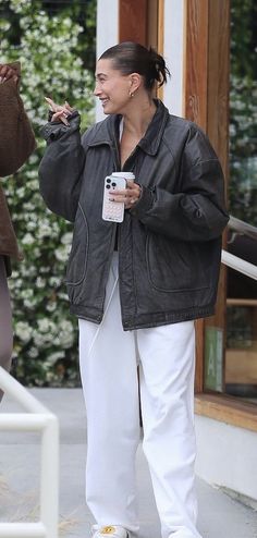 a woman in white pants and black jacket talking on her cell phone while walking down the street