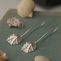 two silver earrings sitting on top of a table next to shells and seashells