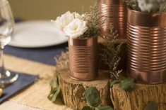 there are many vases with flowers in them on the table top, along with wine glasses and silverware