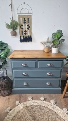 a blue dresser with wooden top and drawers in front of a wall hanging on the wall