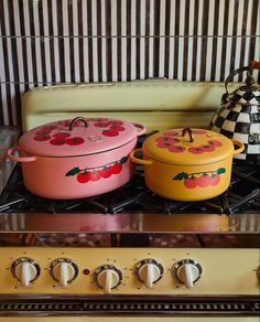 three pots are sitting on top of the stove, one is pink and one is yellow