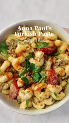 a white bowl filled with pasta covered in meat and vegetables on top of a table