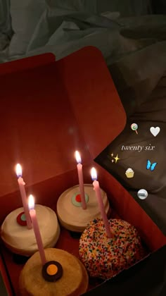 three donuts with lit candles in a red box