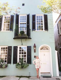 a woman standing in front of a blue building with black shutters and white doors