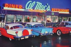 several classic cars are parked in front of a diner at night with the neon lights on