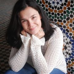 a woman sitting in front of a colorful wall with her hands on her chin and looking at the camera