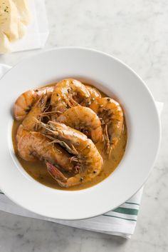 a white plate topped with cooked shrimp and gravy on top of a table