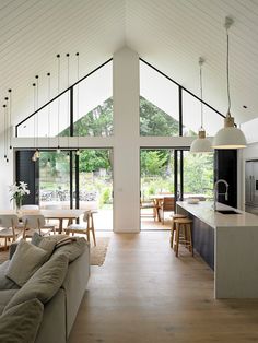 a living room filled with furniture next to an open kitchen and dining area in front of large windows